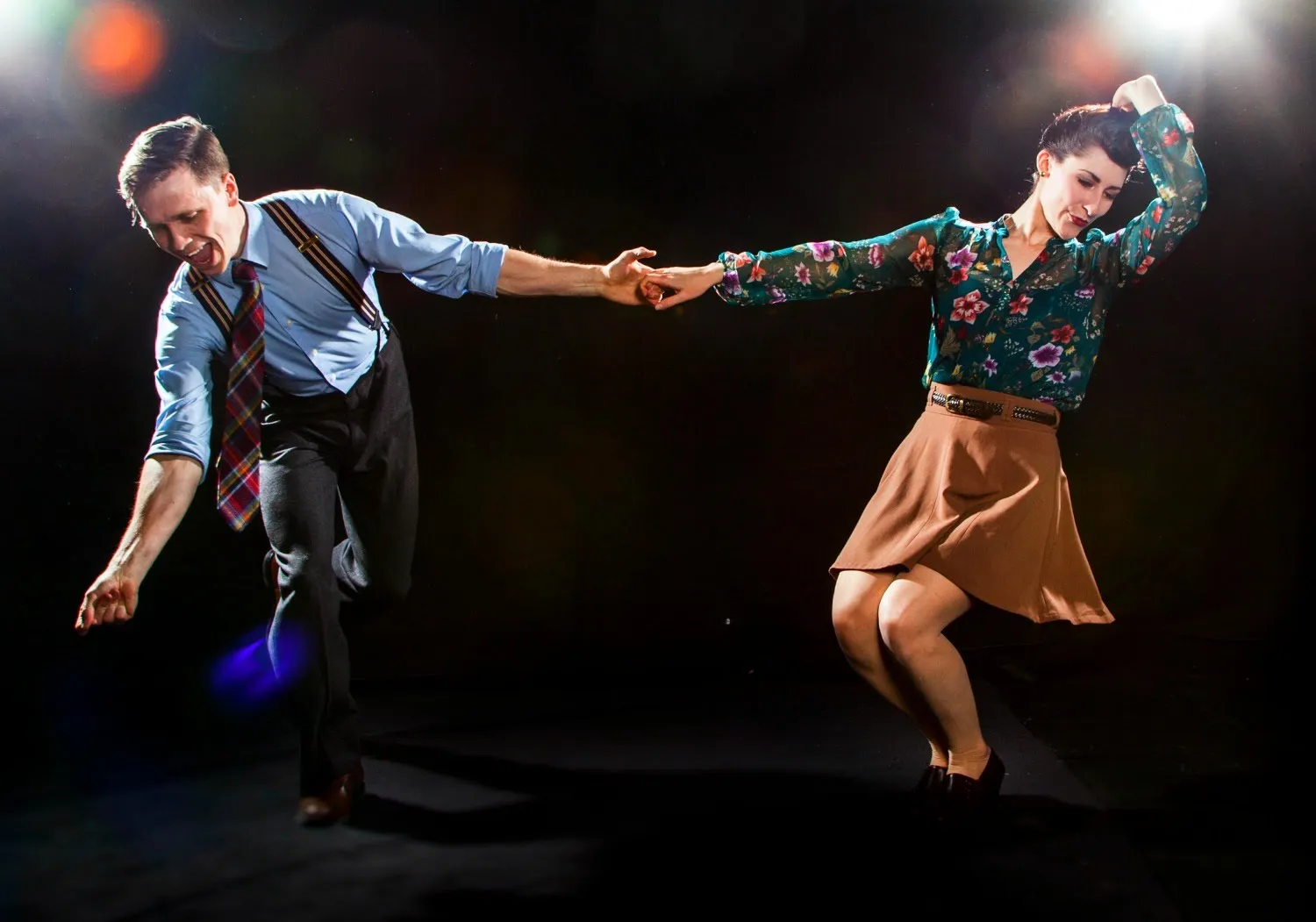 Two ballroom swing dancers dancing under lights.